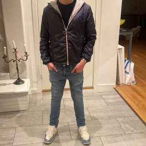 Mörkblå windbreaker från Moncler - Snygg mörkblå vindjacka från Moncler med huva och vit dragkedja. Jackan har en klassisk Moncler-logga på ärmen och grått innerfoder. Perfekt för dig som vill ha en stilren outfit. Passformen är normal och jackan är långärmad. Skicket är nästan perfekt har använt fåtal gånger. Säljer för ska köpa ny! Storlek 164cm.