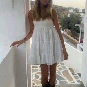 Vit somrig kortklänning med volang - Superfin vit kortklänning med volang och ärmlös design. Klänningen har en luftig passform och smockad överdel.