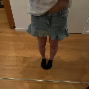 Handgjord Jeanskjol med volang - Säljer en ljusblå handgjord jeanskjol från Gina Tricoti storlek 36. Kjolen är kort och har en snygg volangkant nedtill samt klassiska jeansdetaljer som fickor och knappstängning. Perfekt för dig som gillar denim och vill ha en cool look.