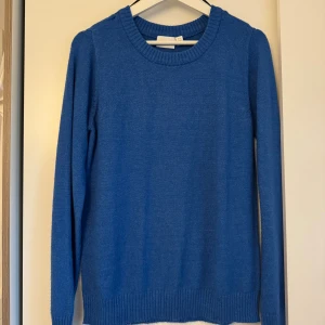 Blå stickad tröja från Vila - Snygg blå stickad tröja från Vila i storlek S. Tröjan har rund halsringning, ribbade muddar vid ärmslut och nederkant samt långärmad passform. Perfekt för dig som gillar enkel och stilren design med en poppig färg.