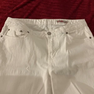 Vita raka jeans från Cue - Snygga vita jeans från Cue med klassisk femficksdesign och raka ben. Byxorna har bälteshällor, silverfärgade nitar och subtil struktur i tyget. Perfekta för dig som vill ha en clean och fräsch look.