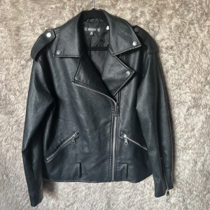 Svart skinnjacka från Missguided - Snygg svart skinnjacka från Missguided med klassisk bikerstil, bred krage och silvriga dragkedjor på fickor och ärmslut. 