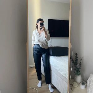 Svarta högmidjade byxor från Amisu - Säljer ett par svarta, högmidjade byxor från Amisu i skinnimitation. Byxorna har raka ben, diskreta sömmar framtill och sidfickor. Materialet är mjukt och ger en cool vibe. Perfekt för dig som gillar minimalistisk stil och vill ha ett statement-plagg i garderoben.