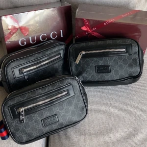 Svart magväska - Snygg svart axelväskamed klassiskt mönster och silverfärgade dragkedjor. Väskan har en rektangulär form, justerbar axelrem och detaljer i skinn. Perfekt för att bära det viktigaste med stil.(ENDAST 1 VÄSKA PER KÖP, ENDAST VÄSKA)