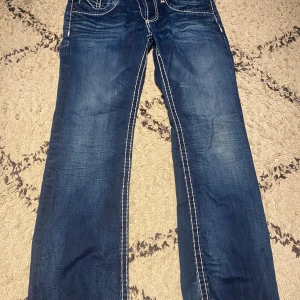 Blå jeans med vita sömmar - Snygga blå jeans med markerade vita kontrastsömmar och klassisk femficksdesign. Jeansen har raka ben och en något lösare passform. Materialet är slitstarkt denim och de har coola slitningar framtill och bakfickor med dekorativa sömmar.