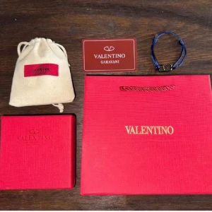 Valentino armband  - Snyggt armband från Valentino Garavani med marinblått band och metallspänne med ikoniska V-loggan. Dustbag o allt på bilden tillkommer. Skick 9/10. Priset är inte hugget i sten 
