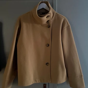 Beige/kamel färgad kappa med hög krage och knappar - Kamel färgad jacka från Gina tricot med hög krage. 