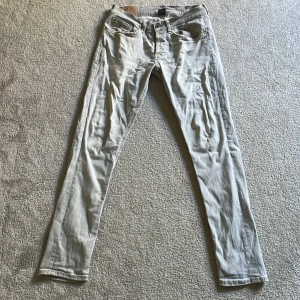 Ljusgrå jeans från Dondup - Säljer ett par ljusgrå jeans från Dondup med klassisk femficksdesign och snygga slitningar. Jeansen har raka ben och är tillverkade i mjukt bomullstyg. Perfekta för dig som gillar en avslappnad och trendig look.