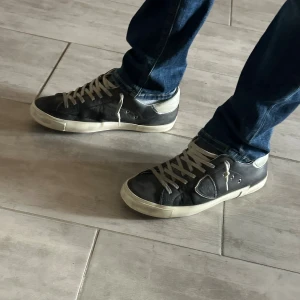 Philippe Model mörkblåa sneakers - Mörk blåa sneakers från Philippe Model med vita detaljer och snörning. Skorna har en rund tå, platt sula och silverfärgad häl med logotyp. Köpt förra sommaren och är välanvända (därför lågt pris) skolåda medföljer köpet. Om du har några andra frågor är det bara att fråga på🙌