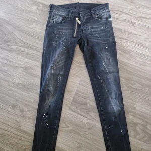 Svarta skinny jeans från Dsquared2 - Snygga svarta skinny jeans från Dsquared2 med coola slitningar och vita färgstänk. Jeansen har dragkedjedetalj framtill och klassisk femficksdesign. Tillverkade i Italien i stretchig bomull för en tight passform.