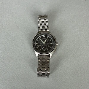 Citizen Eco-Drive silverklocka - Citizen Eco-Drive herrklocka med svart urtavla och silverfärgat armband i metall. Klockan har kronograf, datumvisning och flera små urtavlor. Snygg och stilren design med rund boett och länkarmband som ger en modern vibe.