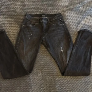 Svarta Replay jeans Wallys - Säljer ett par svarta Replay jeans, modell Wallys. Jeansen har en klassisk femficksdesign, diskreta slitningar framtill och raka ben. Materialet är jeans i bomullsblandning och färgen är mörkgråsvart med lätt tvättad look. Perfekta för dig som gillar en stilren och avslappnad vibe.