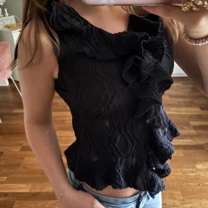 Svart volangblus från Gina Tricot - Säljer en svart blus från Gina Tricot med coolt skrynkligt tyg och volangdetaljer längs fram, jättefin🤍