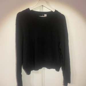 Svart långärmad tröja från Divided - En basic svart långärmad tröja från Divided med rund halsringning och enkel design. Tröjan är i mjuk bomull och har en något lös passform med lätt vågig nederkant. Perfekt att styla med jeans eller kjol.