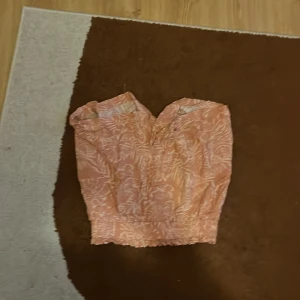 Rosa tubtopp från Angelology XS - Säljer en söt rosa tubtopp från Angelology i storlek XS. Toppen har ett ljust blommigt mönster och är smockad upptill och nedtill för en bekväm passform. Perfekt för varma dagar och har en fräsch, feminin vibe.