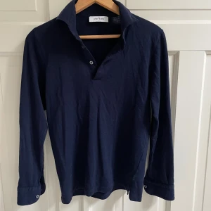 Mörkblå pop over shirt från Gran Sasso - Säljer en mörkblå pop over shirt från Gran Sasso i mjuk ull. Skjortan har lång ärm, klassisk krage och knappar upptill. Perfekt för dig som gillar stilren och enkel design med italiensk känsla. I storlek 46 IT, motsvarande S