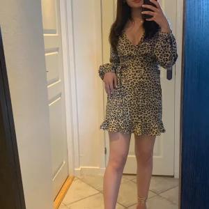 Leopardmönstrad omlottklänning NA-KD - Säljer en snygg kort leopardmönstrad omlottklänning från NA-KD i beige och bruna toner. Klänningen har långa ärmar, v-ringning och knyt i midjan för en schysst passform. Använd 1gg förut. 