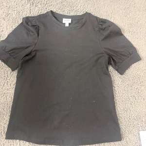Svart blus med puffärm från Vero Moda - Svart blus från AWARE by Vero Moda. Modellen har puffade korta ärmar med rynk vid axeln. Bra skick nästan aldrig andvänd 
