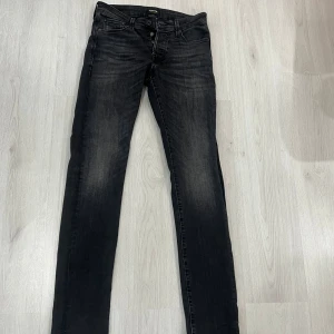Svarta slim jeans Jack & Jones - Svarta jeans från Jack & Jones i modellen Slim/Glenn. Jeansen har en slim passform med smala ben och klassisk femficksdesign. Materialet är stretchigt jeans och färgen är tvättad svart med lätt slitning för en cool look.