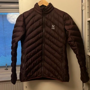 Brun pufferjacka från Haglöfs dam S - Säljer en brun/vinröd pufferjacka från Haglöfs i dammodell, storlek S. Jackan har snyggt mönstrad quiltning, hög krage och dragkedja framtill. Perfekt för kyliga dagar och riktigt skön att bära. Två fickor med dragkedja på sidorna. Nu pris 999