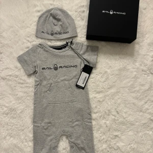 Sail Racing babyset grå 0–6 mån HELT NY i presentbox - Sail Racing babyset, body och mössa i grått. Setet består av en mjuk kortärmad body med ficka framtill och tryckknappar längs benen, samt en matchande mössa med loggan framtill. Storlek: 0–6 månader 100% bomull 🌟 Helt nytt med tag kvar! 🌟 Kommer i original presentförpackning  Perfekt som present 🩶 Finns i fler färger och storlekar i mina annonser.