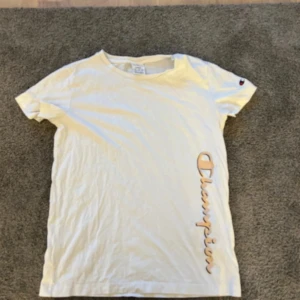 Vit Champion t-shirt med tryck - Vit t-shirt från Champion med korta ärmar och rund hals. Är mer som en S är väldigt liten i storlek.