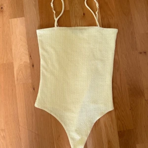 Ljusgul topp från Bik Bok, S - Supersöt gul body från Bik Bok i storlek S. Modellen är en onepiece med smala axelband och ribbad struktur som ger en snygg och modern look. Perfekt för strandhäng och poolparty under sommaren. Materialet känns mjukt och följsamt mot huden.