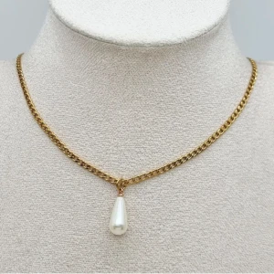Guldhalsband med pärlhänge - Stilrent halsband i guldtonad metall med en kedja och ett droppformat vitt pärlhänge. Kedjan har klassisk länkkonstruktion och pärlan ger en elegant touch. Perfekt för dig som gillar minimalistisk och chic design.