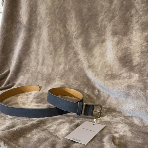 Mörkblått bälte  - Stilrent mörkblått bälte med matt silverfärgat spänne. Bältet har en klassisk, rak form och är gjort i skinn med ljusbrun insida. Perfekt accessoar för att lyfta din outfit. 100cm