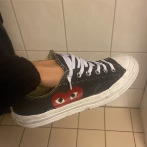 Converse x CDG Play svarta sneakers - Svarta Converse sneakers i samarbete med Comme des Garçons Play. Klassisk låg modell med vit tå, vita snören och den ikoniska röda hjärtloggan med ögon på sidan. Ovandel i canvas och sula i gummi. Perfekta för dig som gillar streetstyle och vill sticka ut.