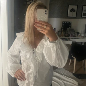 Vit volangskjorta från 157, stl S - Aldrig använt. Säljer en vit skjorta från 157 i storlek S. Skjortan har långa puffärmar, volangdetaljer längs v-ringningen och snörning framtill. Tillverkad i ett lätt och luftigt bomullstyg.