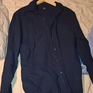 Mörkblå skjorta från Uniqlo, S - En stilren mörkblå skjorta från Uniqlo i storlek S. Skjortan har klassisk krage, knäppning framtill och långa ärmar. Perfekt för dig som gillar en clean och enkel look. Materialet känns mjukt och bekvämt mot huden.