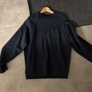 Mörkblå sweatshirt från J.Lindeberg - En stilren mörkblå sweatshirt från J.Lindeberg med diskret logga på bröstet. Tröjan har rund hals, långa ärmar och en klassisk passform. Aldrig använd och säljer pga att den är för stor