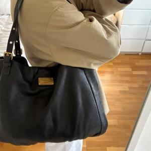 Lädertote Q Classic Shopgirl Tote!  - Snyggaste mörkbruna handväskan i äkta läder från Marc by Marc Jacobs. Den ikoniska modellen Q Classic Shopgirl Tote! En populär och eftertraktad väska med gulddetaljer och dubbla handtag.  Lädret är mjukt, slitstarkt och i mycket fint skick med endast småsmå spår av användning (se bild).  Det här är en klassisk och rymlig modell som inte längre tillverkas, vilket gör den extra eftertraktad. Passar perfekt för dig som vill ha en stilren väska med hög kvalitet och riktigt bra andrahandsvärde🤎