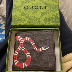 Plånbok med monogram och röd orm - Snygg svart plånbok med ett coolt ormmotiv i rött, vitt och blått på framsidan. Plånboken är tillverkad i skinn och har flera fack för kort och ID. Kommer i original grön box med mönster. Perfekt för dig som vill ha något unikt och stilrent.