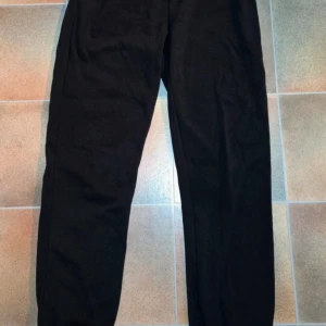 Svarta Mjukisbyxor / Joggers EPCollection - Varma & Bekväma (Strl 34/36) - Säljer ett par klassiska svarta sweatpants (mjukisbyxor/joggers) från EP Collection. Byxorna är varma och bekväma med resår i midjan och dragsko för justerbar passform. De har en bekväm, lite lösare passform och muddar vid anklarna. Perfekta som ett basplagg för hemmamys, avslappnad vardag eller för lättare träning. Märke: EP Collection Storlek: Märkt DAM 34/36 (motsvarar XS/S). Färg: Svart Detaljer: Resår och dragsko i midjan, muddar vid anklarna, har fickor.