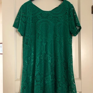 Grön spetstunika med kort ärm - Säljer en grön tunika med korta ärmar och rund hals. Klänningen har ett detaljerat spetsmönster med cirklar och är tillverkad i ett lätt material som ger en luftig känsla. Passformen är normal och längden är kort, perfekt för dig som gillar färg och snygga detaljer.