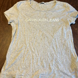 Calvin Klein Jeans t-shirt - grå t-shirt från Calvin Klein Jeans i storlek XL. T-shirten har korta ärmar, rund halsringning och vit logotyptext framtill. 
