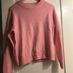Rosa stickad tröja från Vero Moda - Mysig rosa stickad tröja från Vero Moda i storlek M. Tröjan har en rund halsringning, långa ärmar och ribbade muddar vid ärmslut och nederkant. Perfekt för lager-på-lager under kyliga dagar.