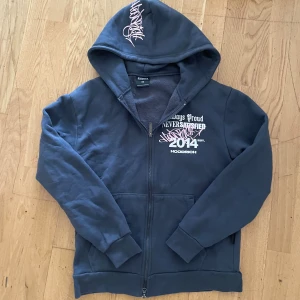 Svart hoodie från Hoodrich med tryck - Streetinspirerad svart hoodie från Hoodrich med stora vita och rosa tryck både fram och bak. Dragkedja framtill, huva och ribbade muddar. Snyggt statement-plagg med text och graffiti-detaljer. Perfekt för dig som gillar urban stil.