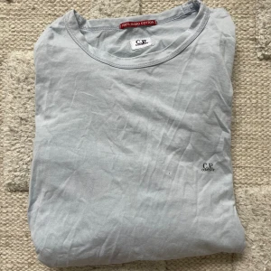 Ljusbrå långärmad tröja C.P. Company - Snygg ljusgrå långärmad tröja från C.P. Company i 100% mako bomull. Enkel design med rund hals och diskret logga på bröstet. Perfekt för chill dagar eller när du vill ha en clean look. Passar dig som gillar stilrena plagg med skön passform.