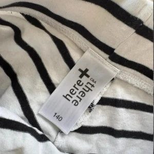 Randiga shorts från here+there C&A - Säljer ett par vita shorts med svarta ränder från here+there C&A. De har en klassisk randig design och är tillverkade i mjuk bomull, perfekta för varma dagar. Shortsen har en bekväm passform och elastisk midja.