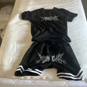 Svart t-shirt med tryck och vita detaljer - Svart t-shirt i polyester med coolt vitt grafiskt tryck på bröstet. Klassisk rund hals och korta ärmar. Passar perfekt till streetwear och har en loose fit. Materialet är lätt och skönt, och de vita detaljerna ger en sportig vibe.