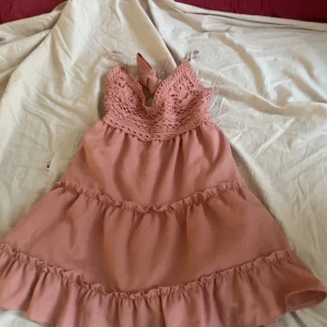 Rosa kortklänning med spets och volanger - Supersöt rosa kortklänning med spets upptill och volanger nertill. Klänningen har knytband i ryggen och är ärmlös med fina detaljer. Perfekt för sommarens alla tillfällen när du vill känna dig extra fin. Endast testad 1 gång och inte använd lapp sitter fortfarande på💞pris kan diskuteras!💞