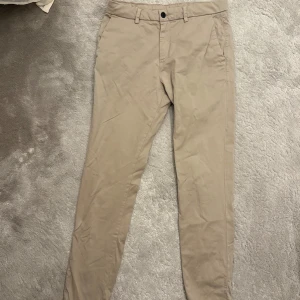 Beiga chinos med raka ben - Snygga beiga chinos med raka ben och klassisk passform. Byxorna har bälteshällor, sidfickor fram och två bakfickor med knapp. Perfekta för en clean och stilren look. Tillverkade i mjuk bomull för skön känsla hela dagen.