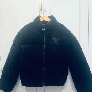 Svart pufferjacka från Juicy Couture - Mysig svart pufferjacka från Juicy Couture med broderad logga på bröstet. Jackan har hög krage, dragkedja framtill och är tillverkad i ett mjukt sammetstyg. Perfekt för kalla dagar när du vill vara både varm och snygg. Bara använd 2-3Gånger. Nypris2800kr