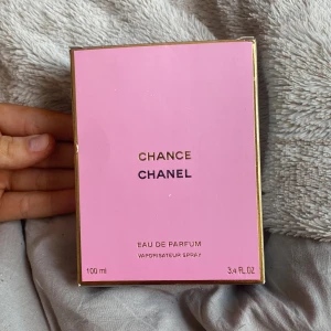 Chanel Chance Eau de Parfum 100ml - Chanel Chance Eau de Parfum i 100 ml flaska. Parfymen kommer i en rund glasflaska med ljusrosa vätska och genomskinlig, fyrkantig kork med Chanel-logga. Ytterkartongen är rosa med gulddetaljer och svart text. En ikonisk och lyxig doft från Chanel.