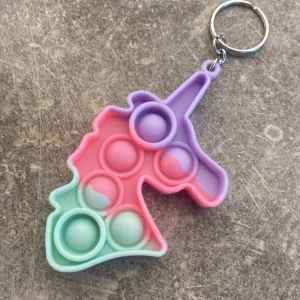 Pastellfärgad enhörning pop it nyckelring - Söt pop it nyckelring i form av en enhörning med pastellfärger i lila, rosa och mintgrönt. Perfekt att hänga på väskan eller nycklarna för en lekfull touch. Tillverkad i mjuk syntet och har flera bubblor att trycka på.