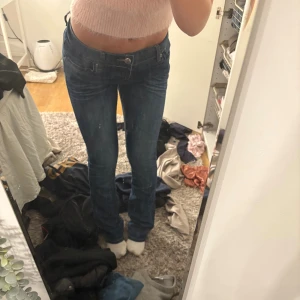 Blå lågmidjade jeans med broderad ficka - Säljer ett par blå jeans med låg midja och klassisk femficksdesign. Jeansen har en snygg broderad detalj på bakfickan och är i en rak modell med lätt tvättade partier. Perfekta för dig som gillar en tidlös och avslappnad look. W27, L34