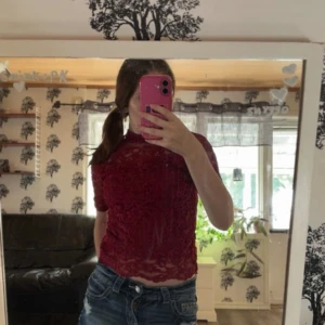 Vinröd spetsblus från H&M  - Säljer en vinröd blus från H&M i storlek S. Blusen är helt i spets med blommigt mönster och har korta ärmar. Den är lätt transparent och har en slim passform som sitter snyggt. Perfekt för dig som gillar detaljer och vill sticka ut lite extra.